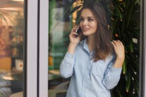 A young, professional woman is talking to a client on her cell phone outside of an office and smiling.