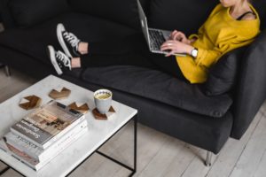 Woman sitting on couch, feet up. Her laptop is on her lap as she types, focused