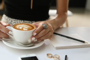 A woman is waiting for her client with a large latte in a cup, complete with a foam flower in the middle of the drink.