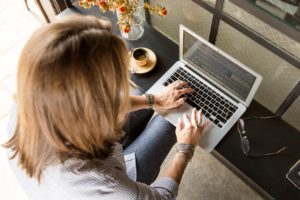 A woman is at her laptop, typing.