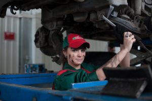 One of "the boys club", the young woman in this picture is wearing a uniform for an auto mechanic shop while working on a car's engine.