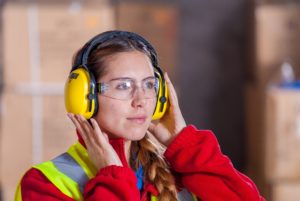 A female mechanic protects her hearing with specialized covered headphones in a loud auto shop