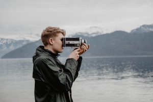 A young man is standing on what looks like a seashore during a very high tide! He's capturing the 'perfect' shot on his vintage film reel... and he's out there all by himself. 