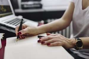 A woman with red painted nails and fancy pen, add notes to a document at her desk